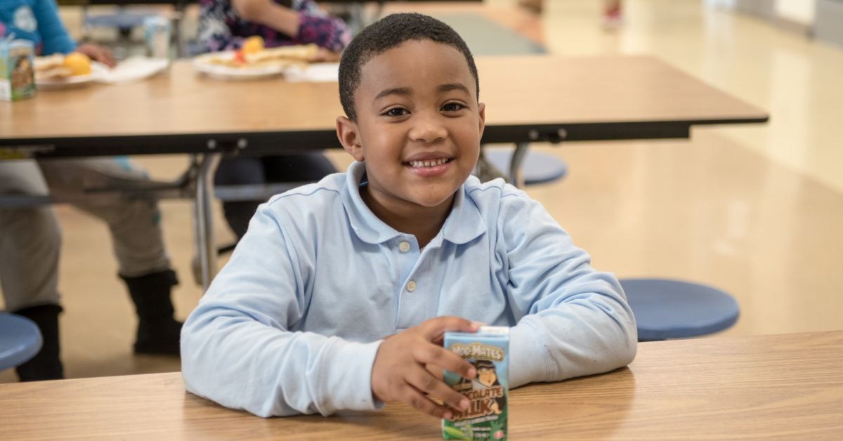 Smiling boy with a carton of milk at a Feed More Kids Cafe program site that provides healthy food supporting child nutrition.