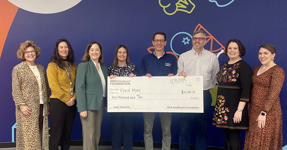 HCA Healthcare and Feed More representatives pose with HCA Healthcare donation in front of Feed More selfie wall.
