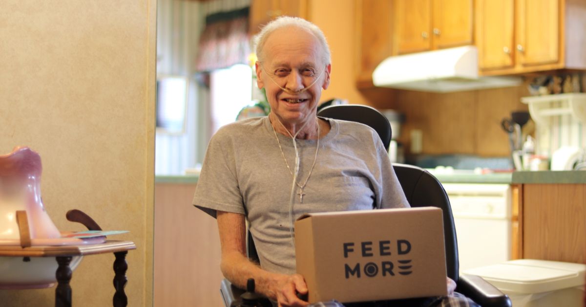 Smiling older man in a wheelchair with a Feed More Meals on Wheels box in his lap sharing his personal journey.