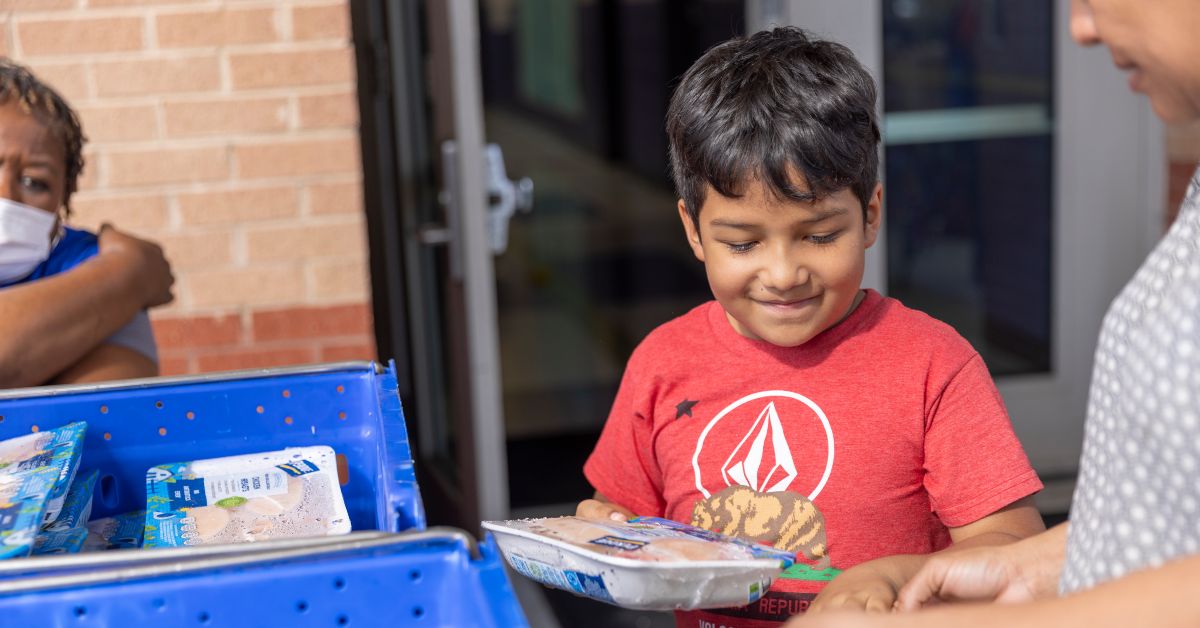 Smiling boy wearing red shirt putting Perdue Farms chicken into a bag at a Feed More partner agency.
