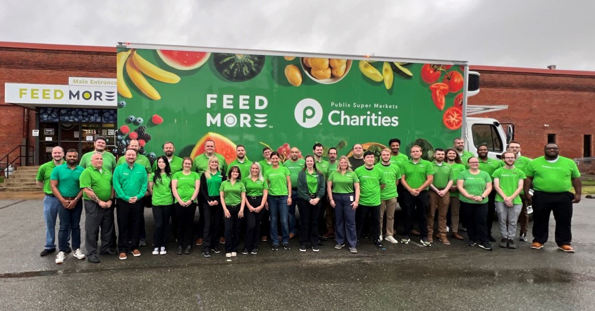 Large group of people wearing green Publix shirts standing in front of a Feed More truck with Publix Super Markets Charities logo.