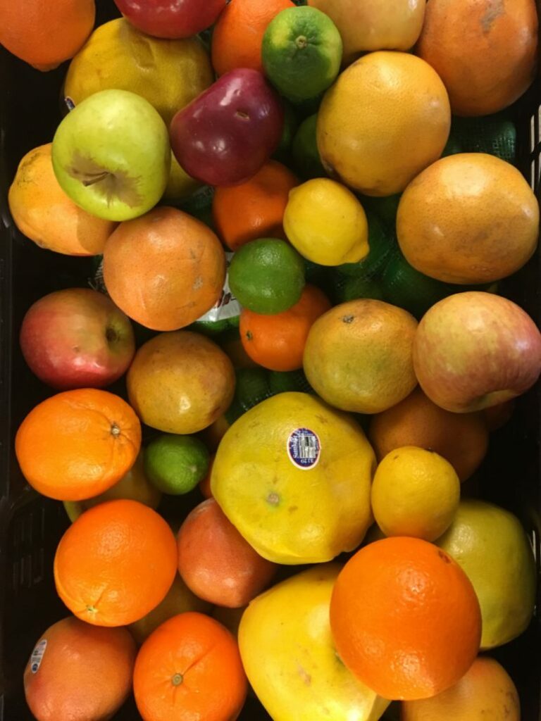 A variety of fresh fruits including apples, oranges, lemons, and limes in a bin, ready for distribution at a Feed More event.