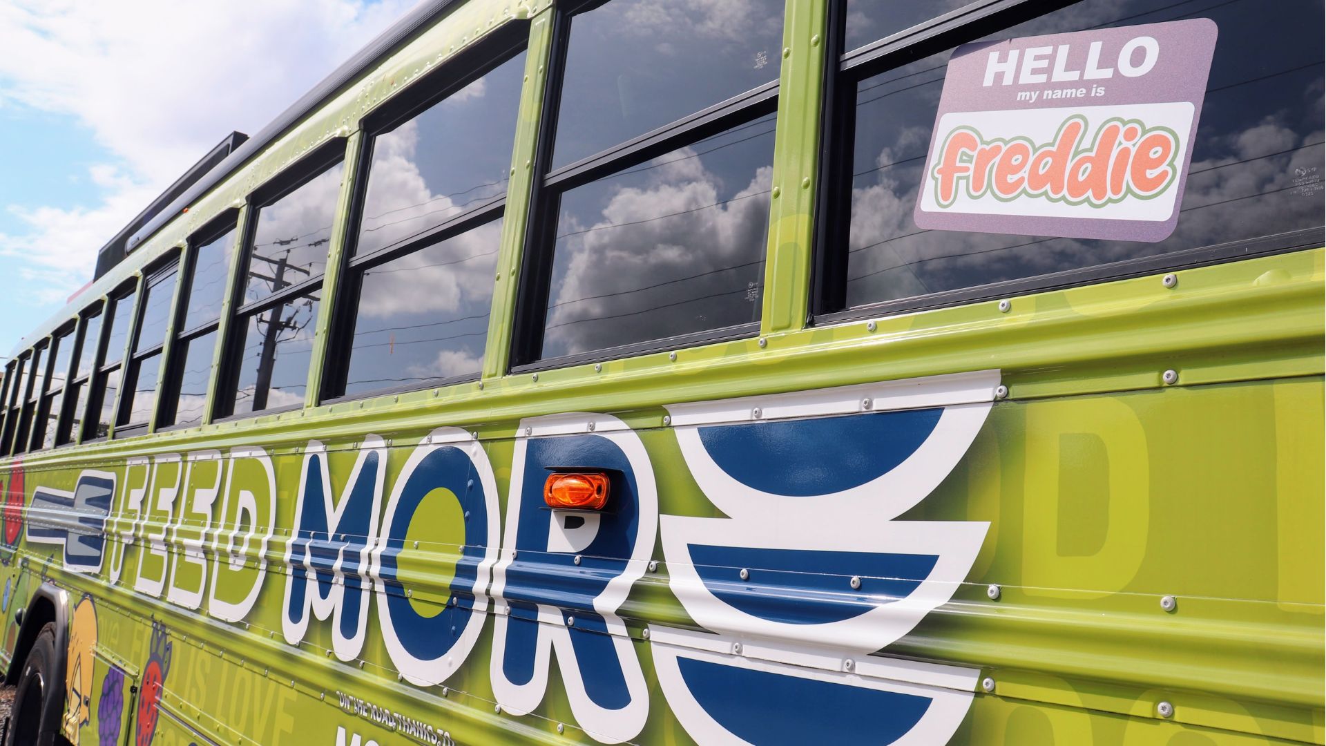 A Feed More bus with the Feed More logo and a 'Hello, my name is Freddie' sticker on the window, showcasing mobile food distribution efforts.